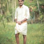 A man stands outdoors in traditional South Indian attire amidst lush greenery, embodying cultural heritage.
